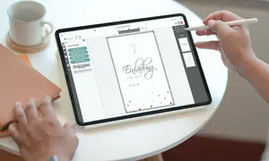 Eine Person bearbeitet eine weiß-graue Einladungskarte zur Taufe des Kindes auf dem iPad mit dem Apple Pencil